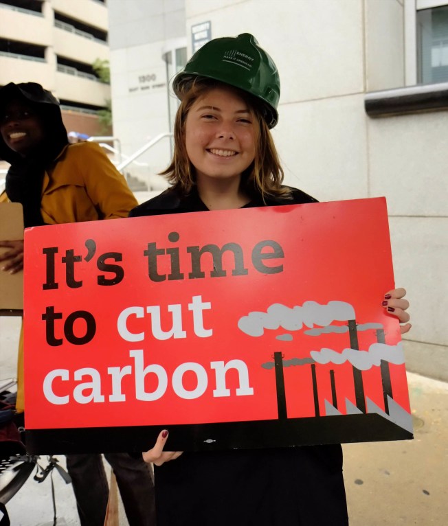 woman holding sign reading It's time to cut carbon